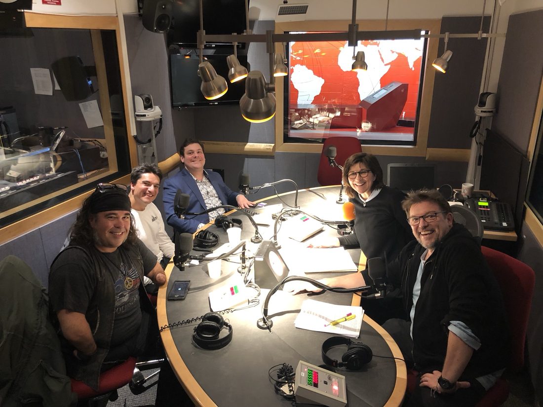 Autour d’une table de studio, avec micros et casques, cinq personnes sourient à l’objectif.