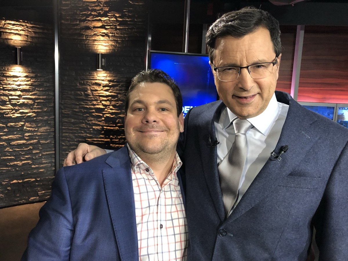 Marc-André Laurier Thibault, en veston bleu, et Denis Lévesque, côte à côte devant un mur de pierre sur un plateau de télévision.